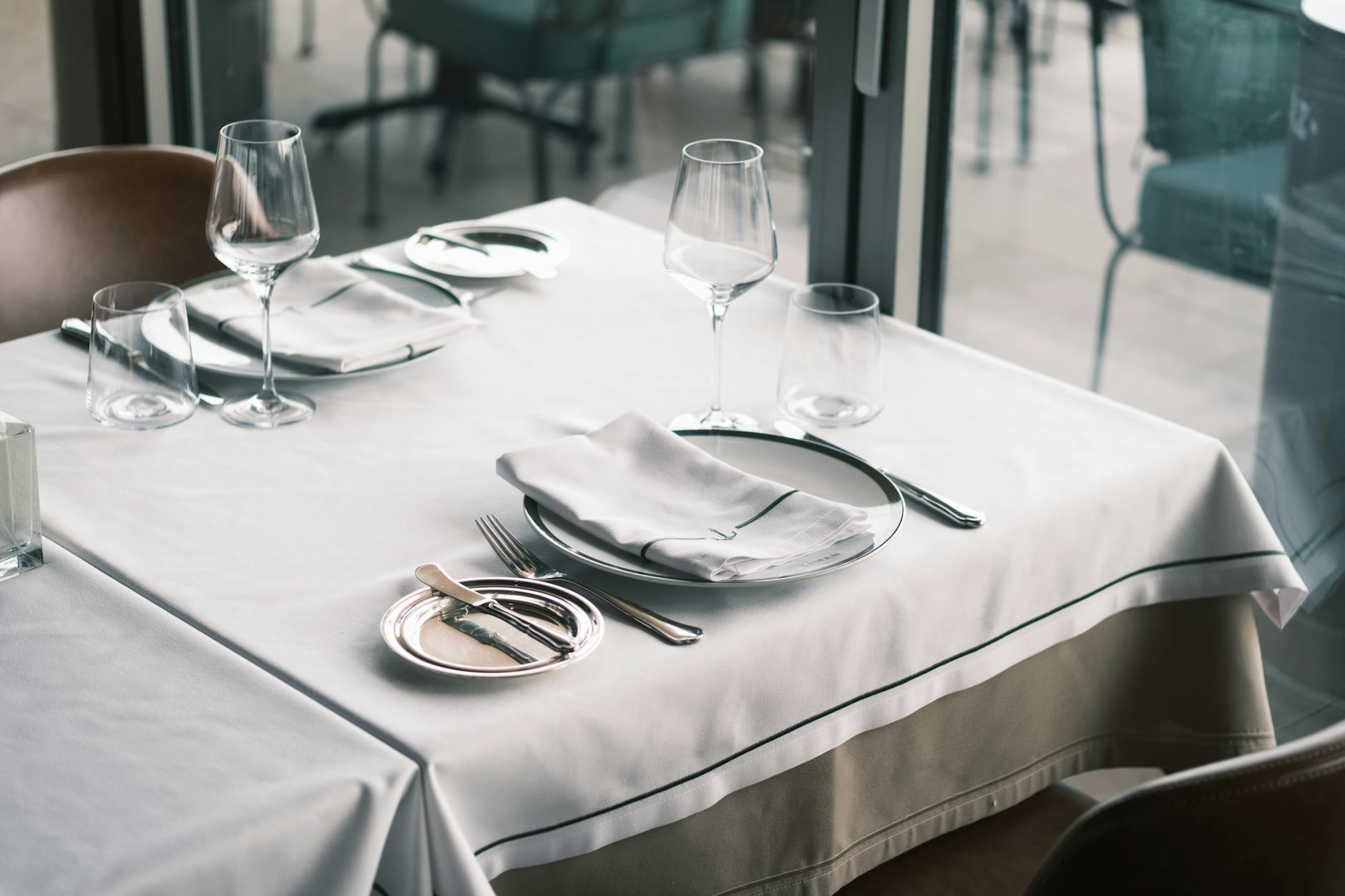 Elegant dining setup with white tablecloths, cutlery, and wine glasses in a modern restaurant setting
