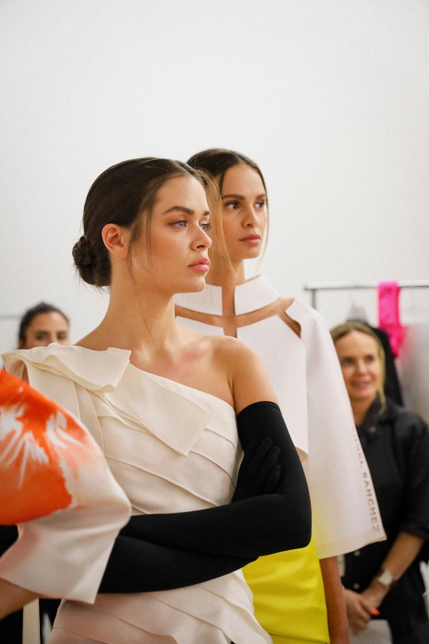 Two models stand backstage at a fashion show in dramatic lighting before a Sydney runway.