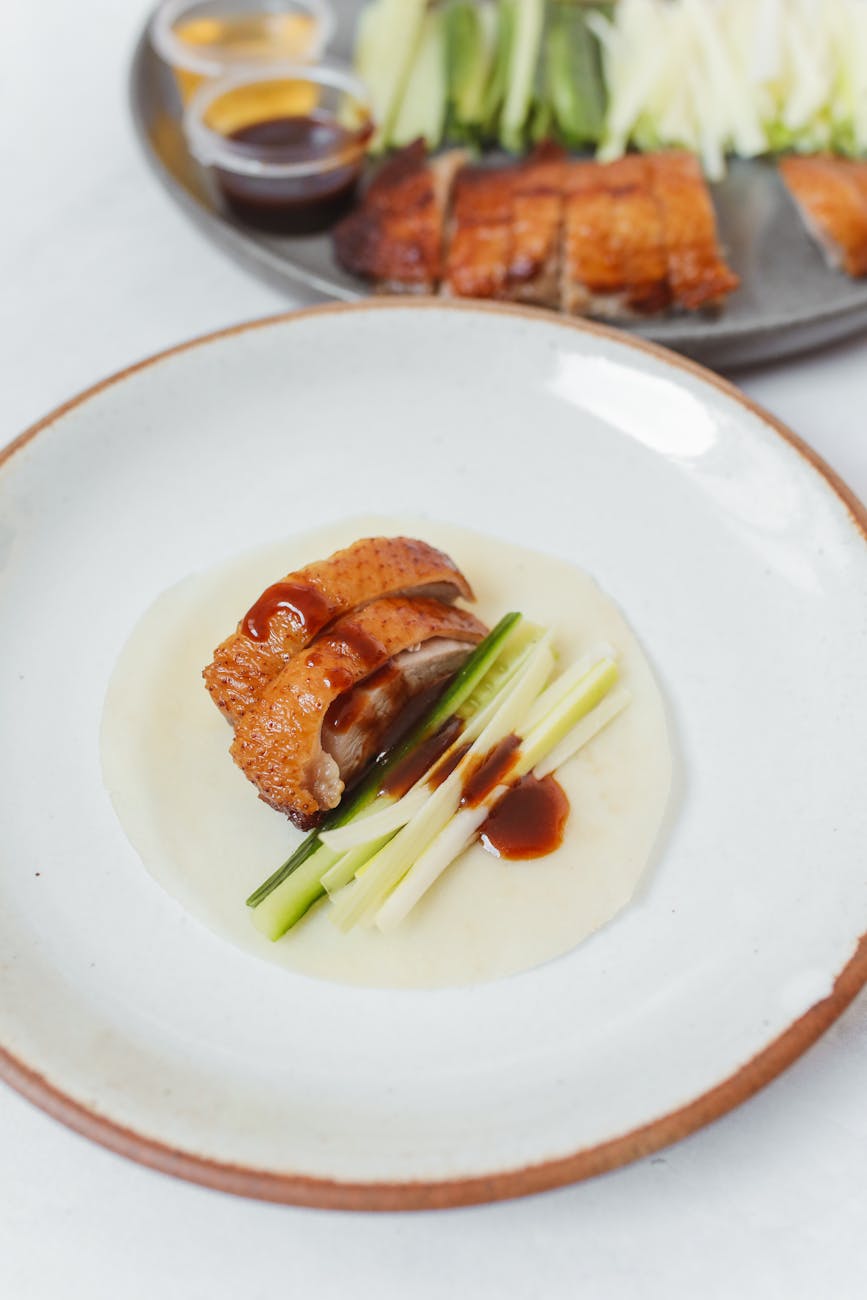 Close-up of Peking duck plated with hoisin sauce, cucumber batons and steamed pancakes on a ceramic bowl
