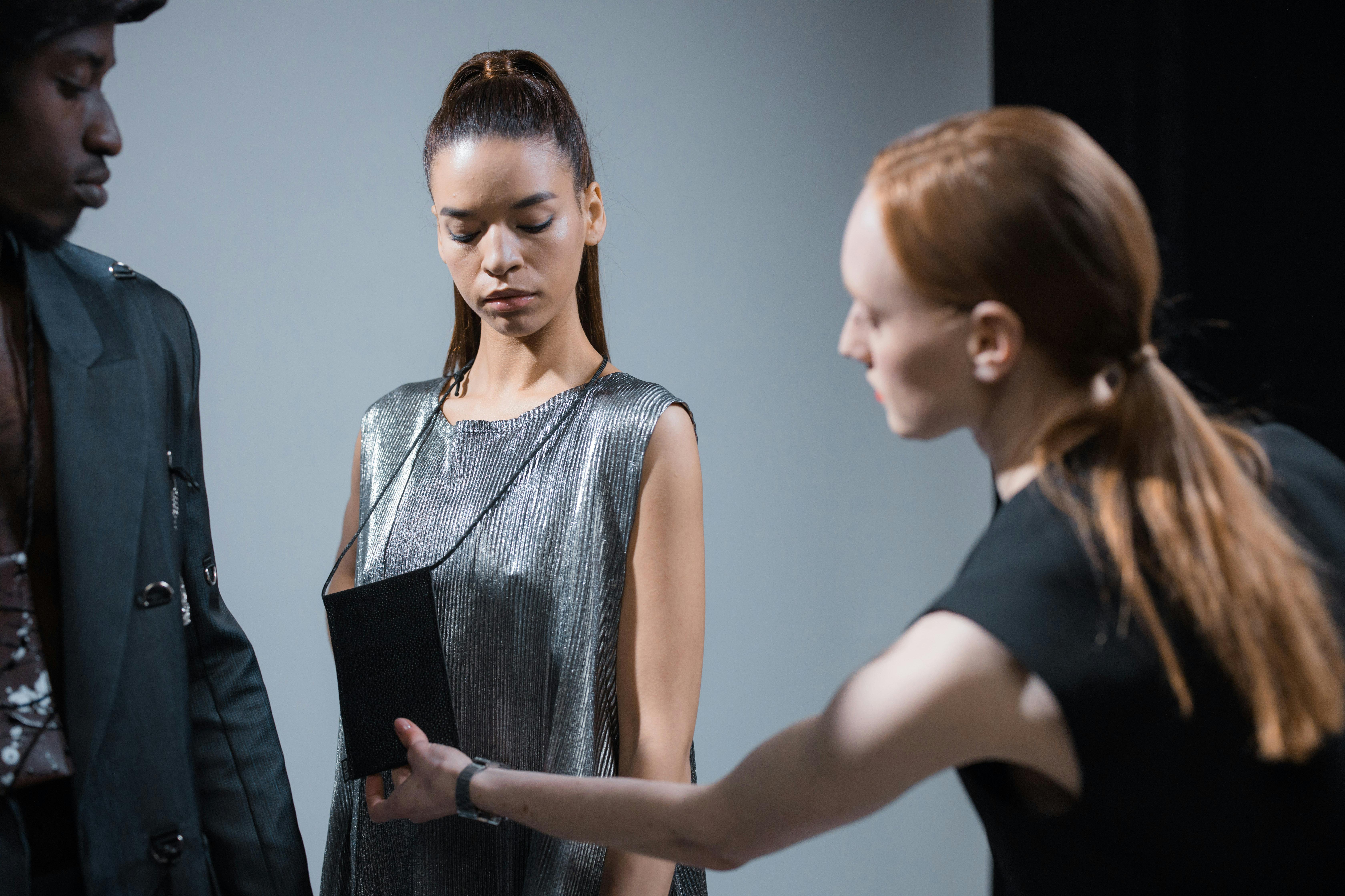 Models preparing backstage at a fashion shoot, designer adjusting garments on a rack