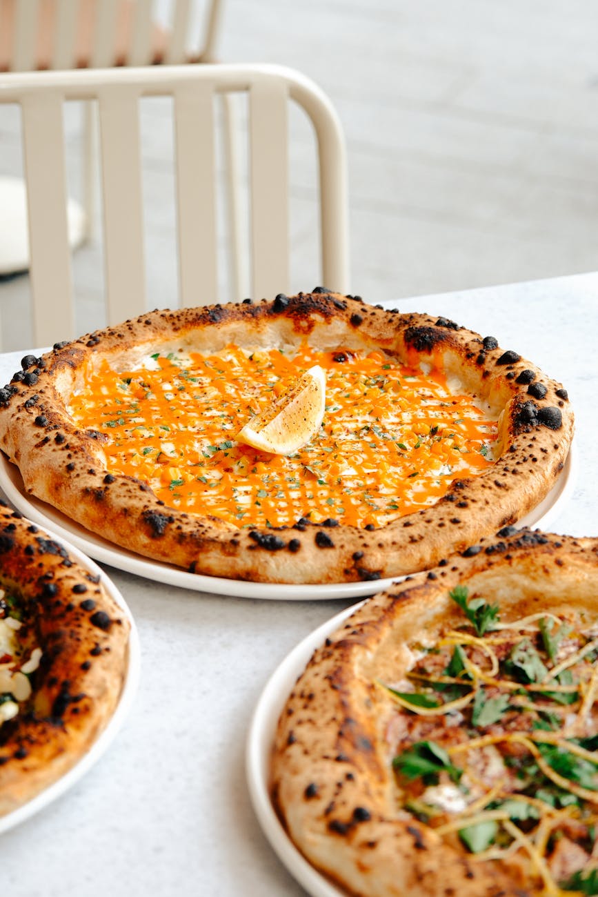 Close-up of artisan pizzas with bright toppings and lemon wedge on a white table.