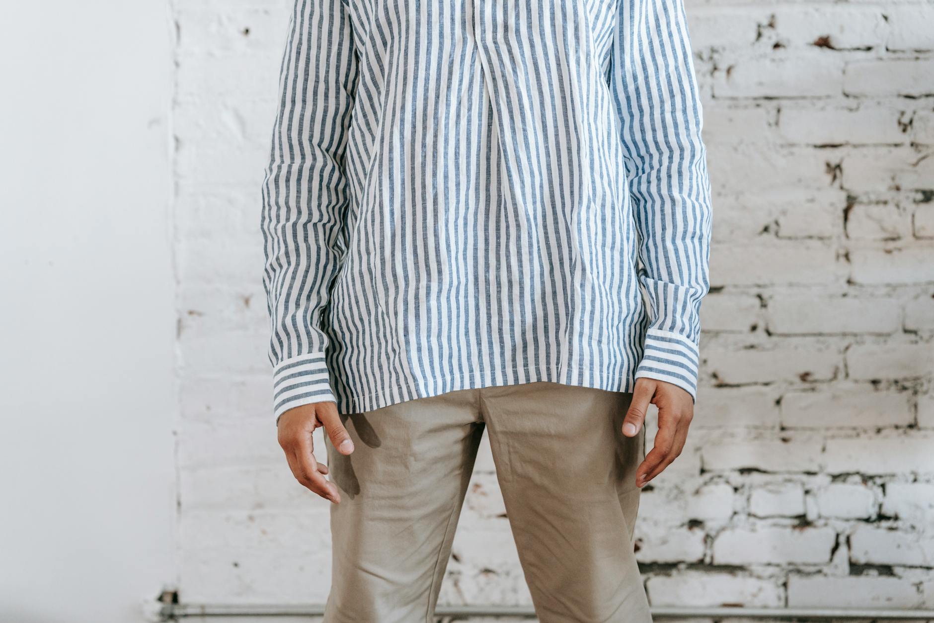 A striped summer shirt with relaxed khaki trousers against a brick wall.