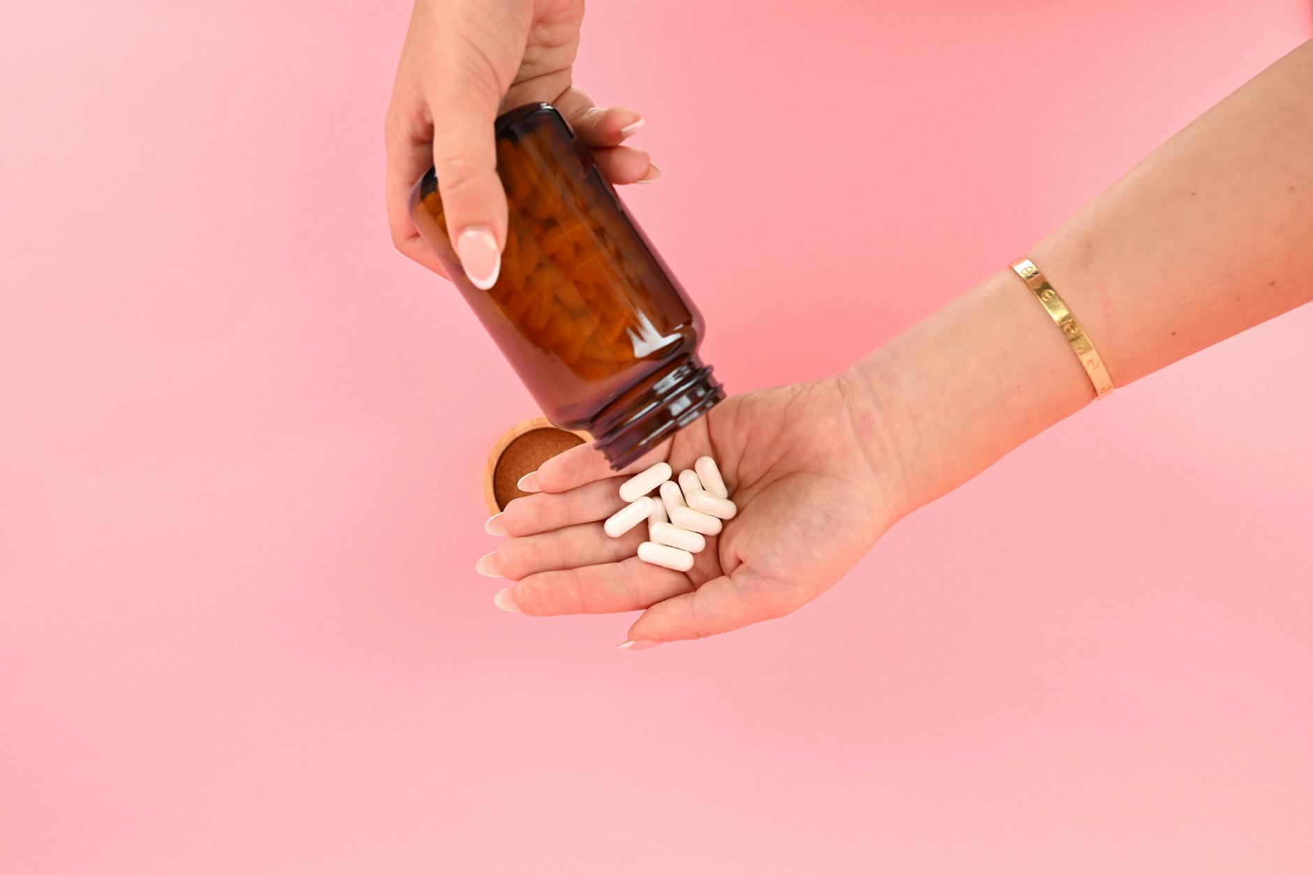Hands tipping white capsules onto a pink background, echoing the beauty-supplement promise of an easy hair-growth fix.
