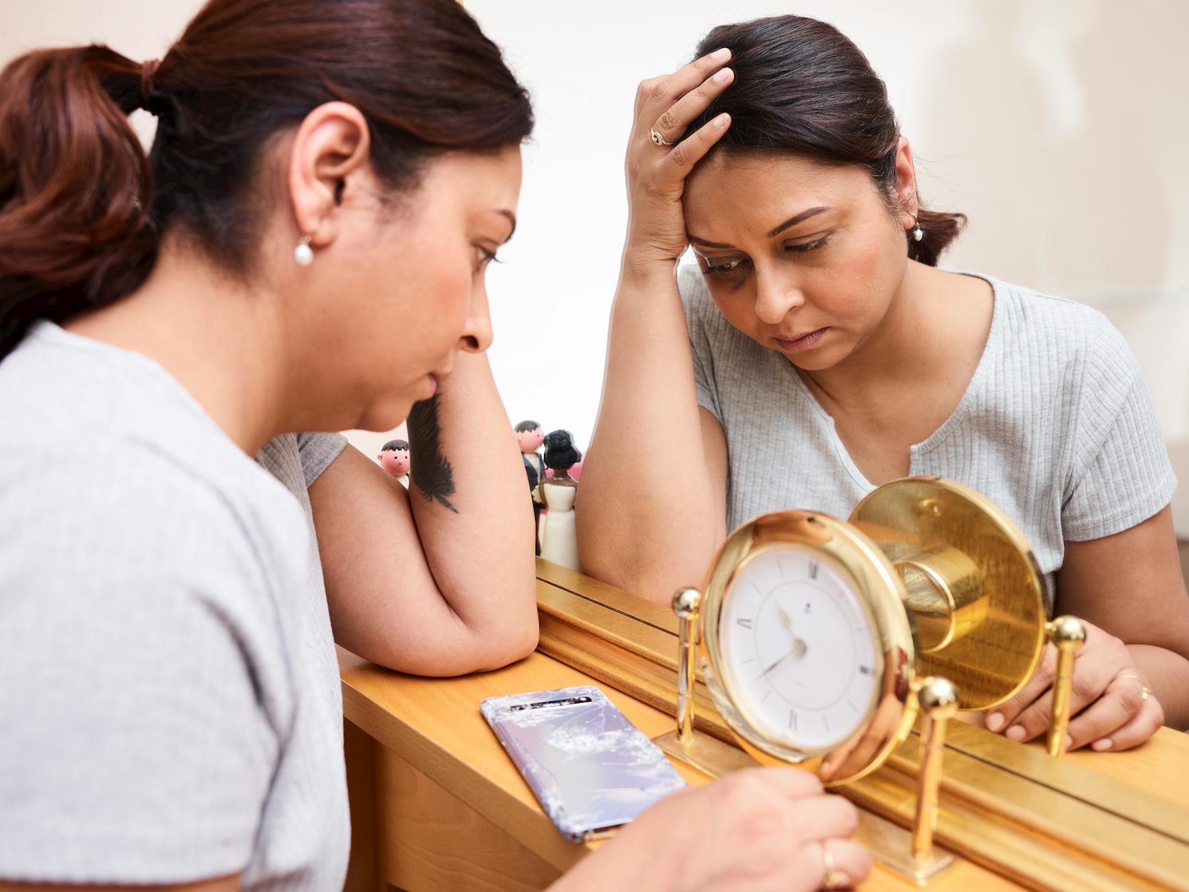 A tired woman sits beside a mirror, capturing the foggy and overcommitted mood that perimenopause marketing often targets.