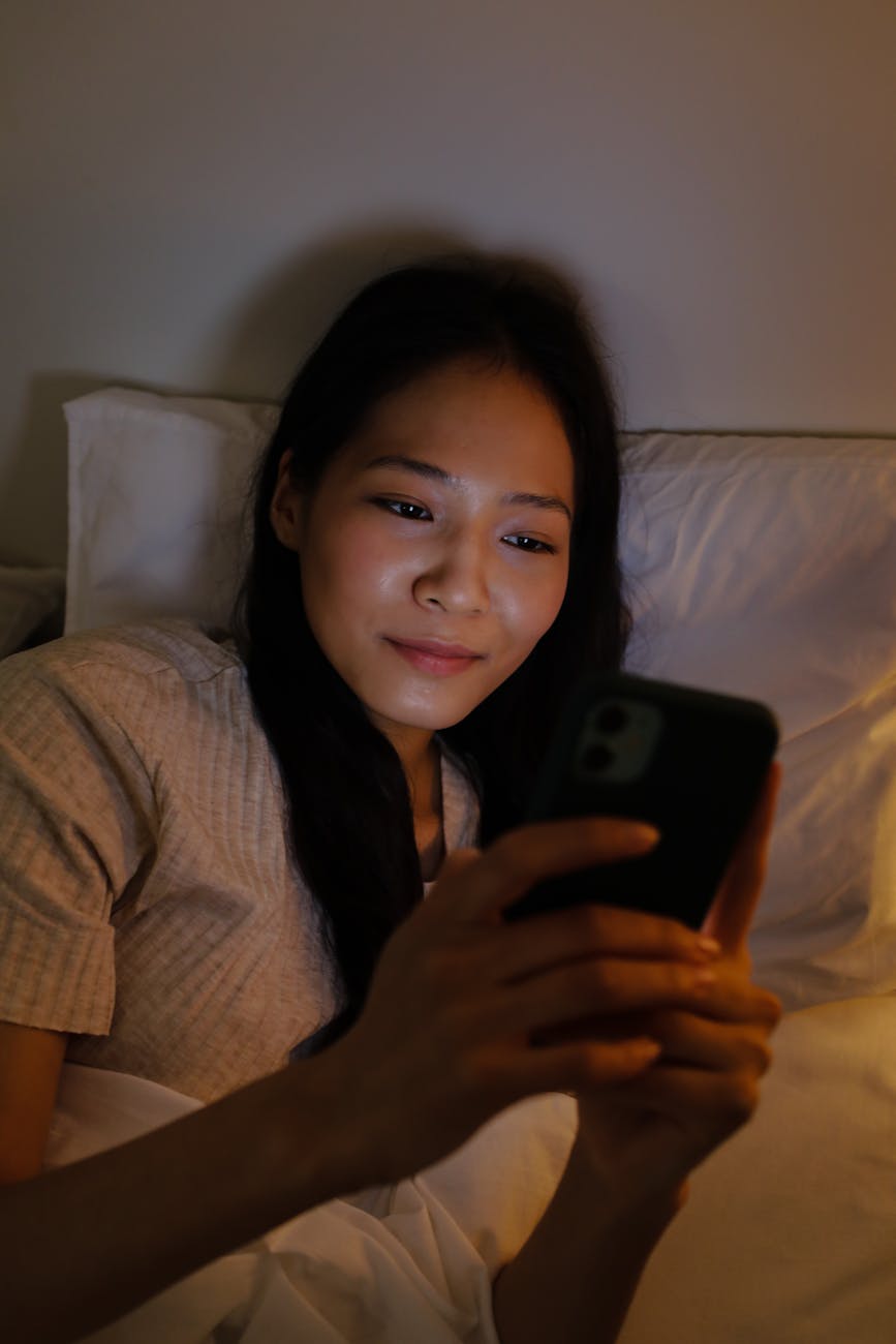 A woman lying in bed lit by her phone, mirroring the late-night scroll the piece opens with.