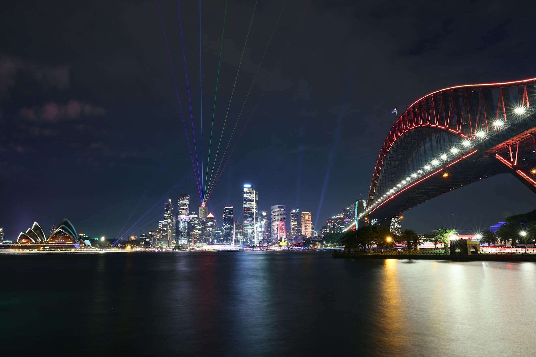 Sydney Harbour glowing at night during festival season, with the Opera House, Harbour Bridge and CBD lit across the water