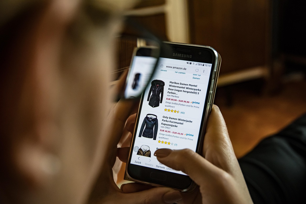 Online shopping on a phone screen beside folded clothing, illustrating the speed of copycat fashion storefronts.