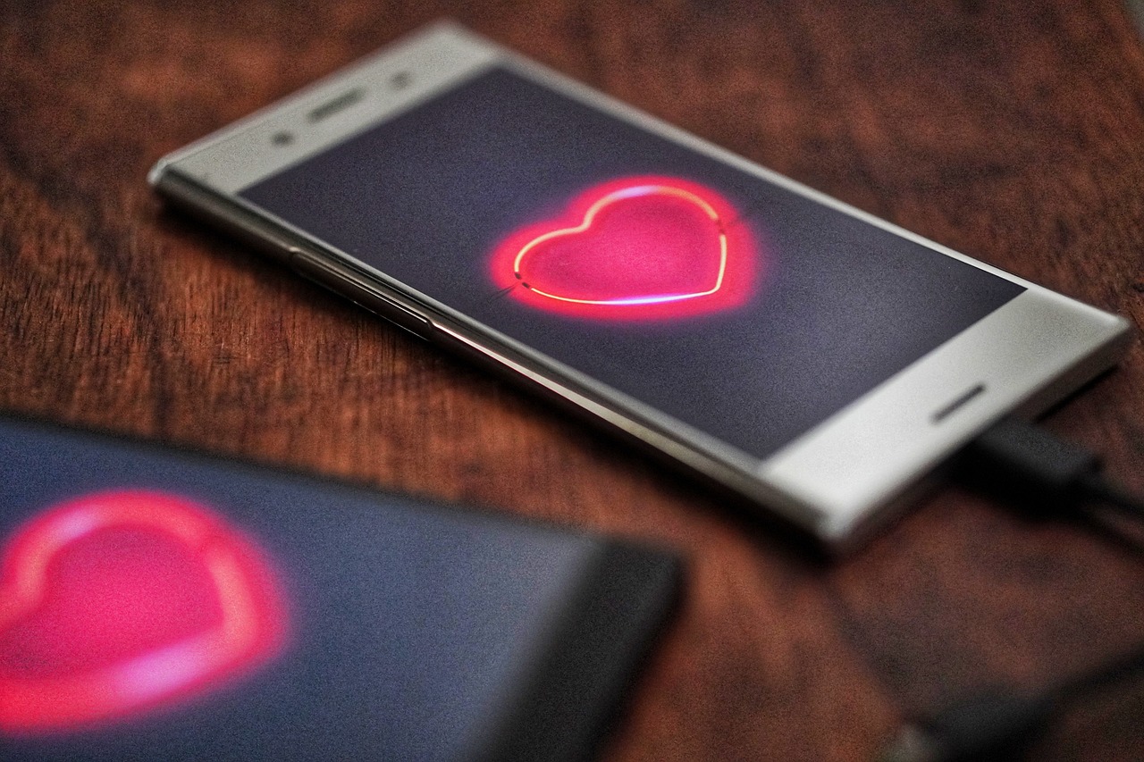 A smartphone displaying a heart icon and phone-based connection, reflecting the gamified logic of modern dating.