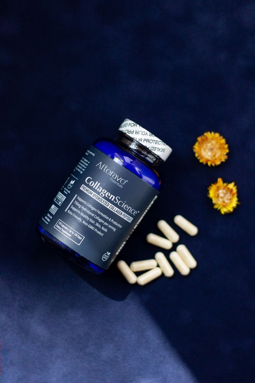 Collagen supplement bottle with capsules and dried flowers on a dark surface.