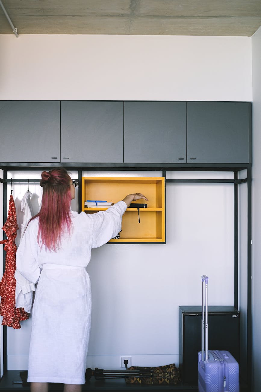 A traveller in a hotel room organising an open suitcase beside the wardrobe