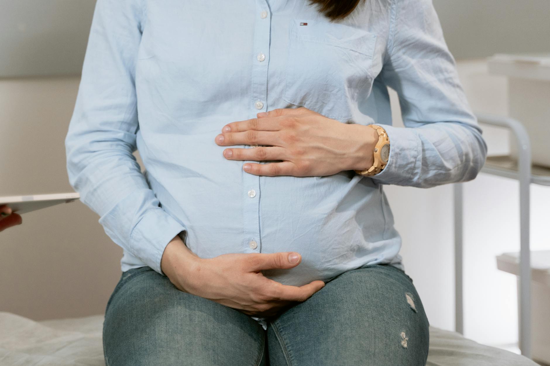 Pregnant woman seated in a clinic, hands resting on her belly during a health conversation