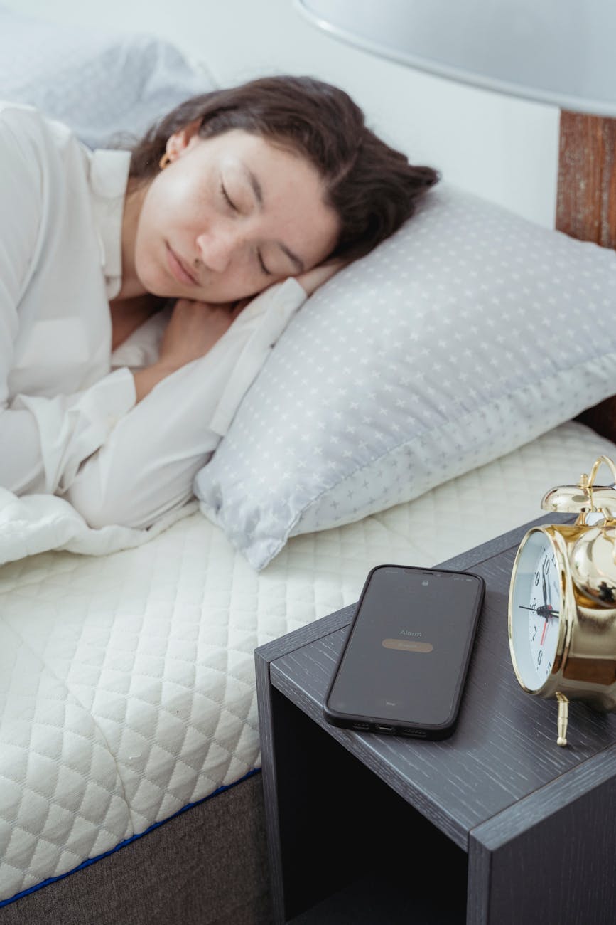 A woman waking beside a smartphone, caught between sleep and the morning’s data.