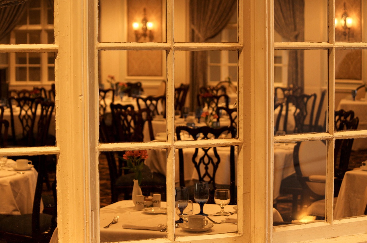 Amber-lit restaurant dining room with tables set beside tall windows