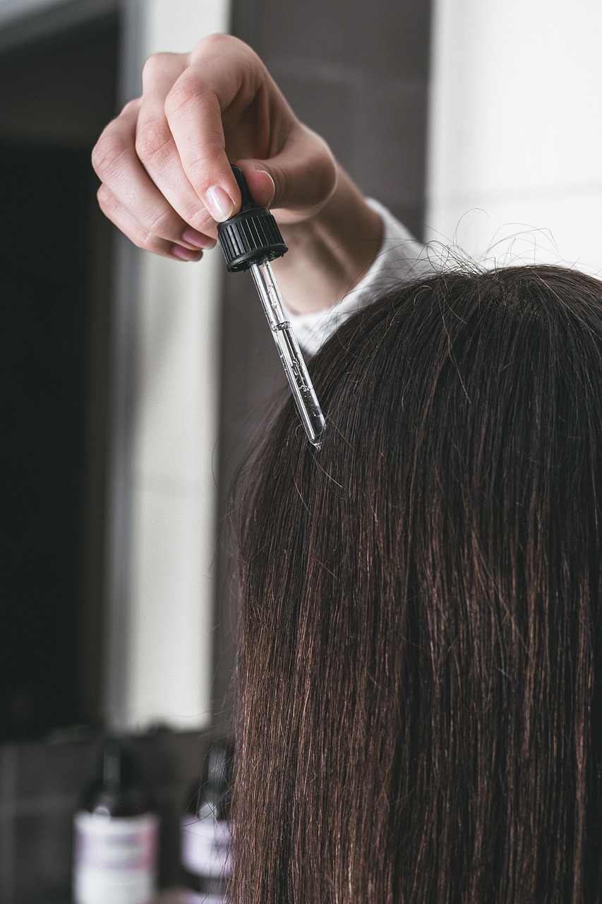 Hair-loss serum bottle held against dark hair, pointing to the private ritual behind scalp-treatment claims.