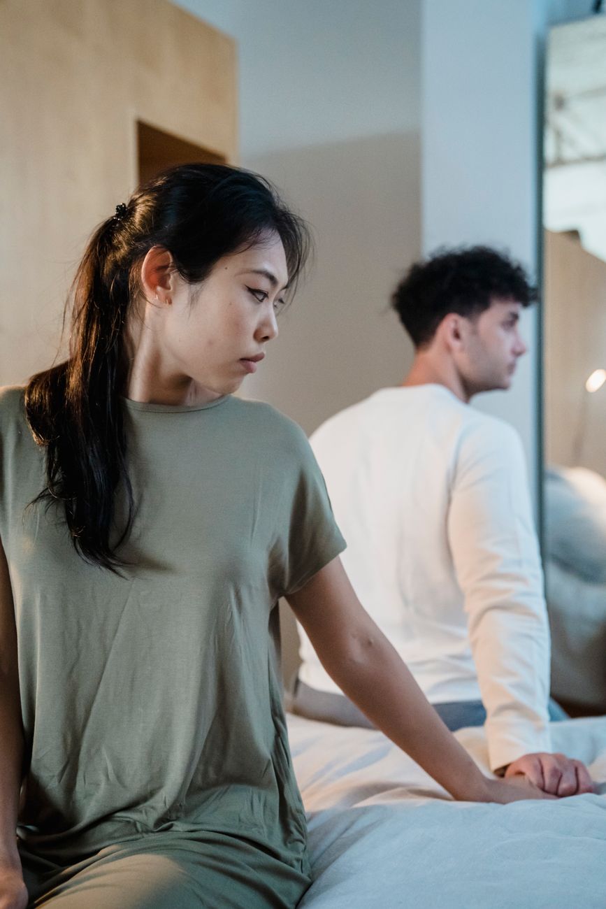 A couple sitting apart on a bed, looking away from each other, echoing the emotional stalemate inside long-term relationships.