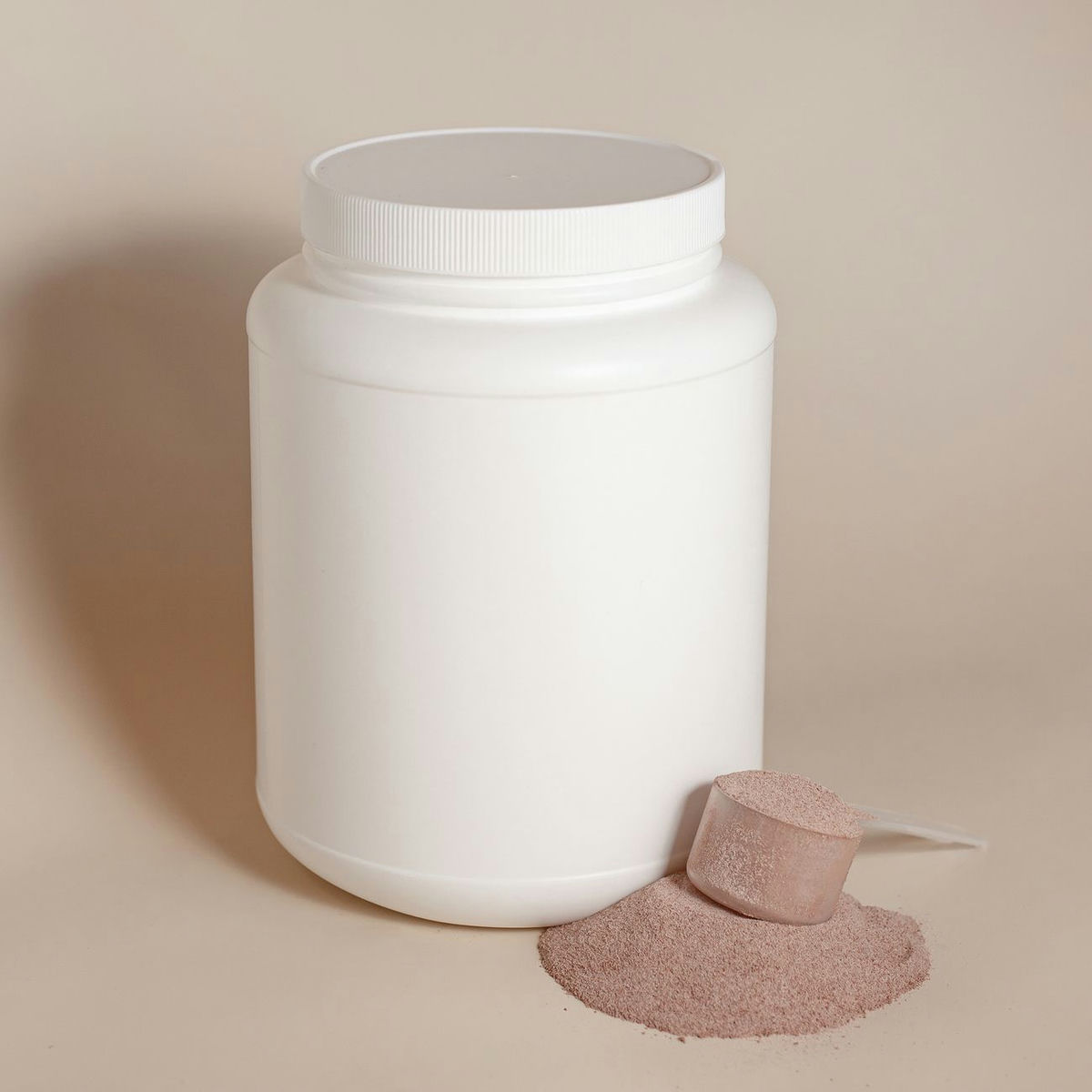 A plain tub of protein powder and a clear scoop sit on a white surface, the old gym format behind today's broader protein market.