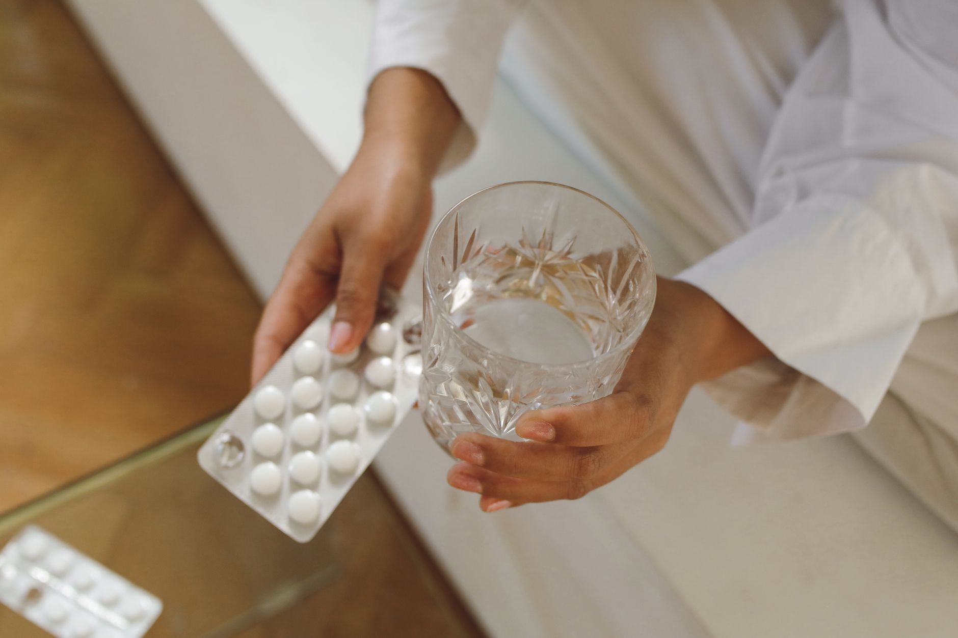 White pills spilling from a bottle beside a glass of water on a bedside surface.
