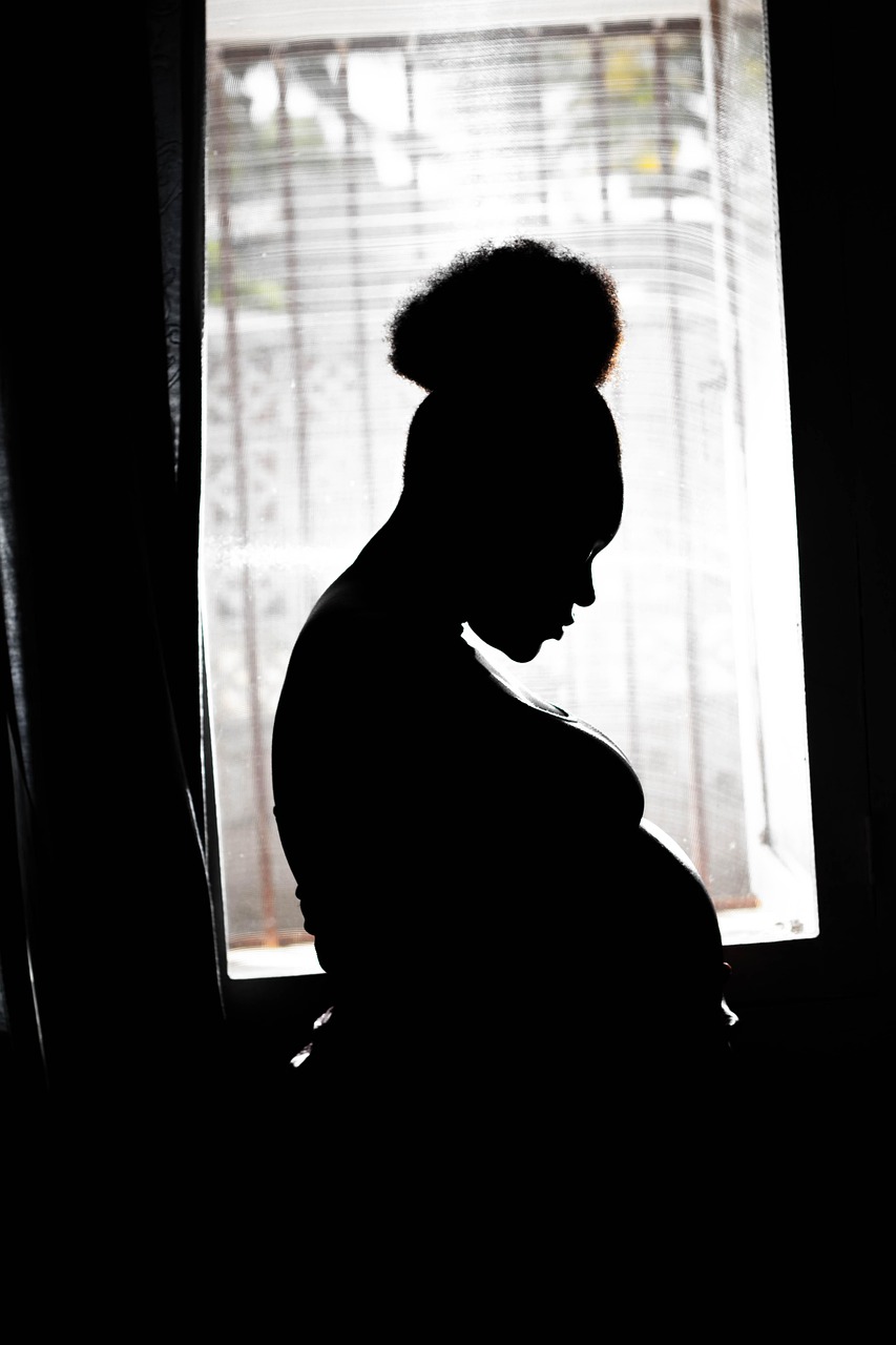 Pregnant woman silhouetted beside a window at home