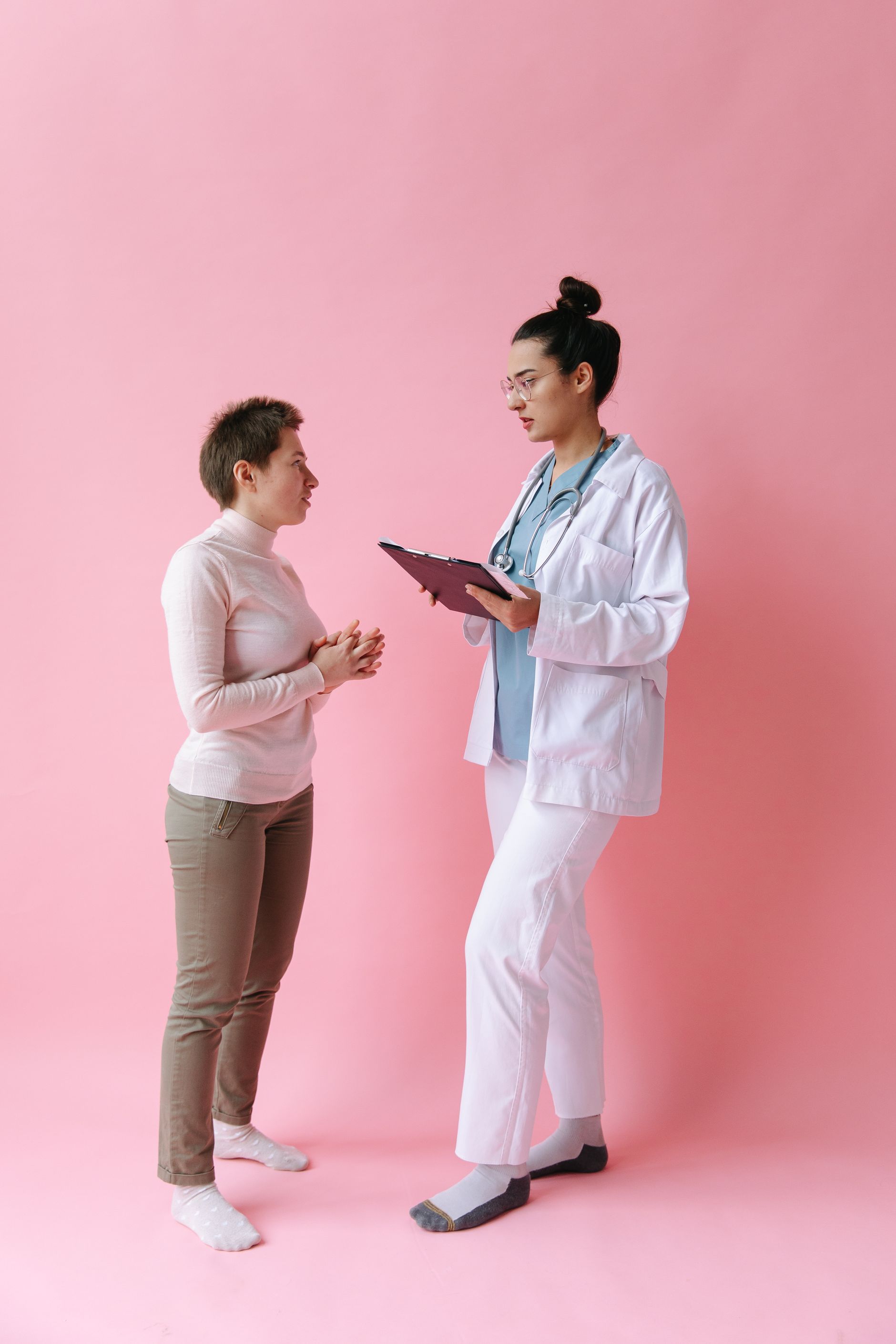 A doctor consulting a patient against a pink backdrop, mirroring the blend of care language and marketing aesthetics in women’s health.