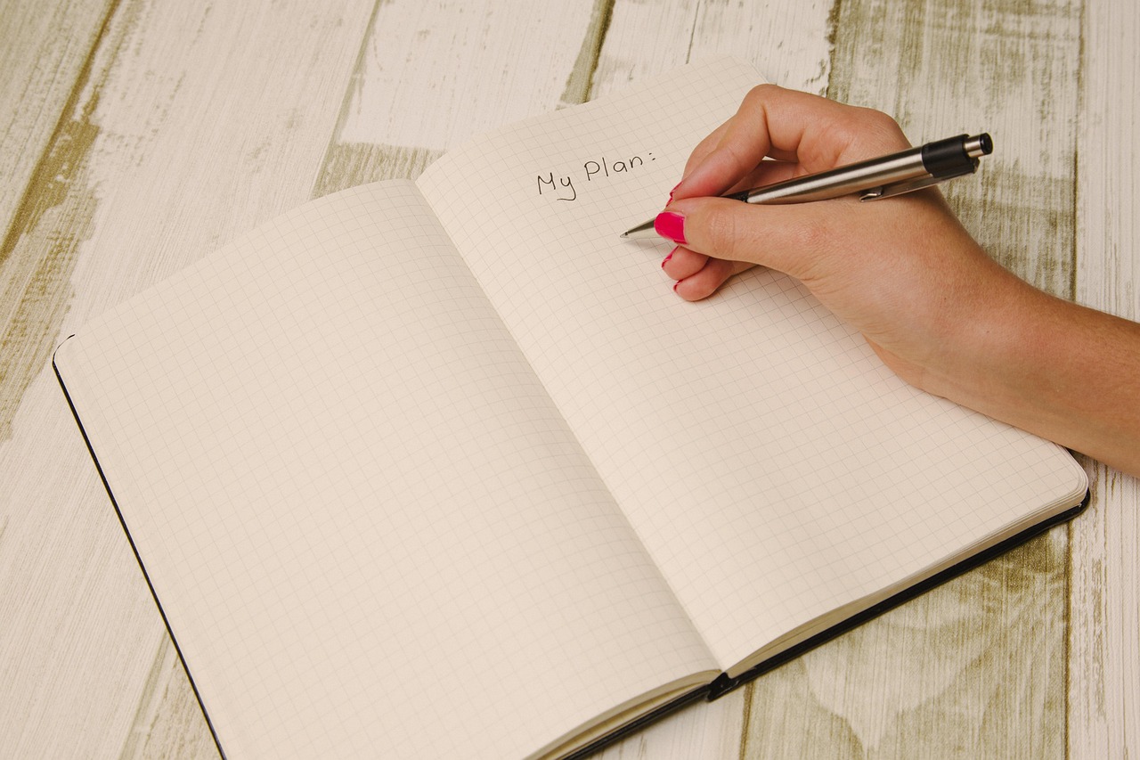 A handwritten planner beside a phone and pen on a desk